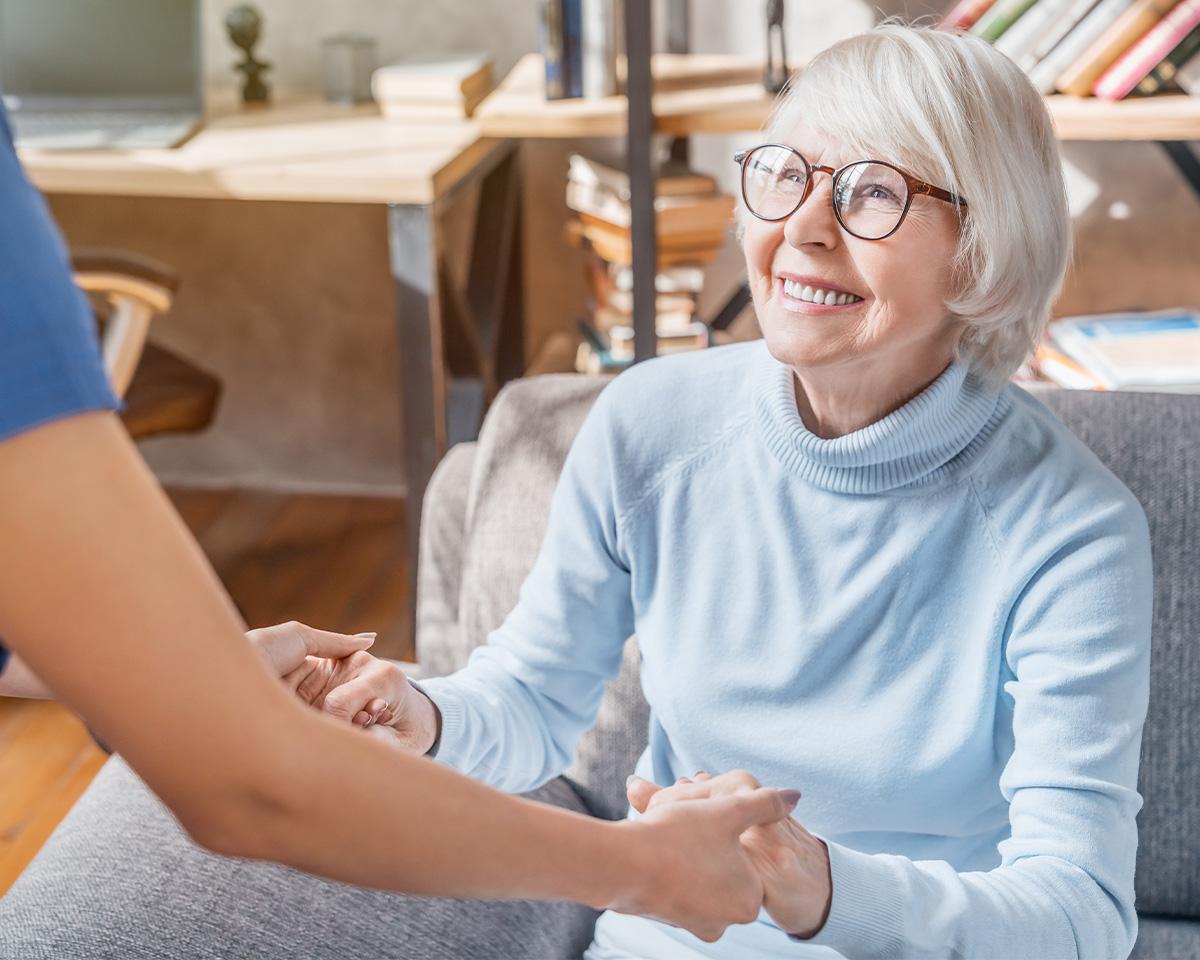 Alltagshelferin hält die Hände einer Seniorin